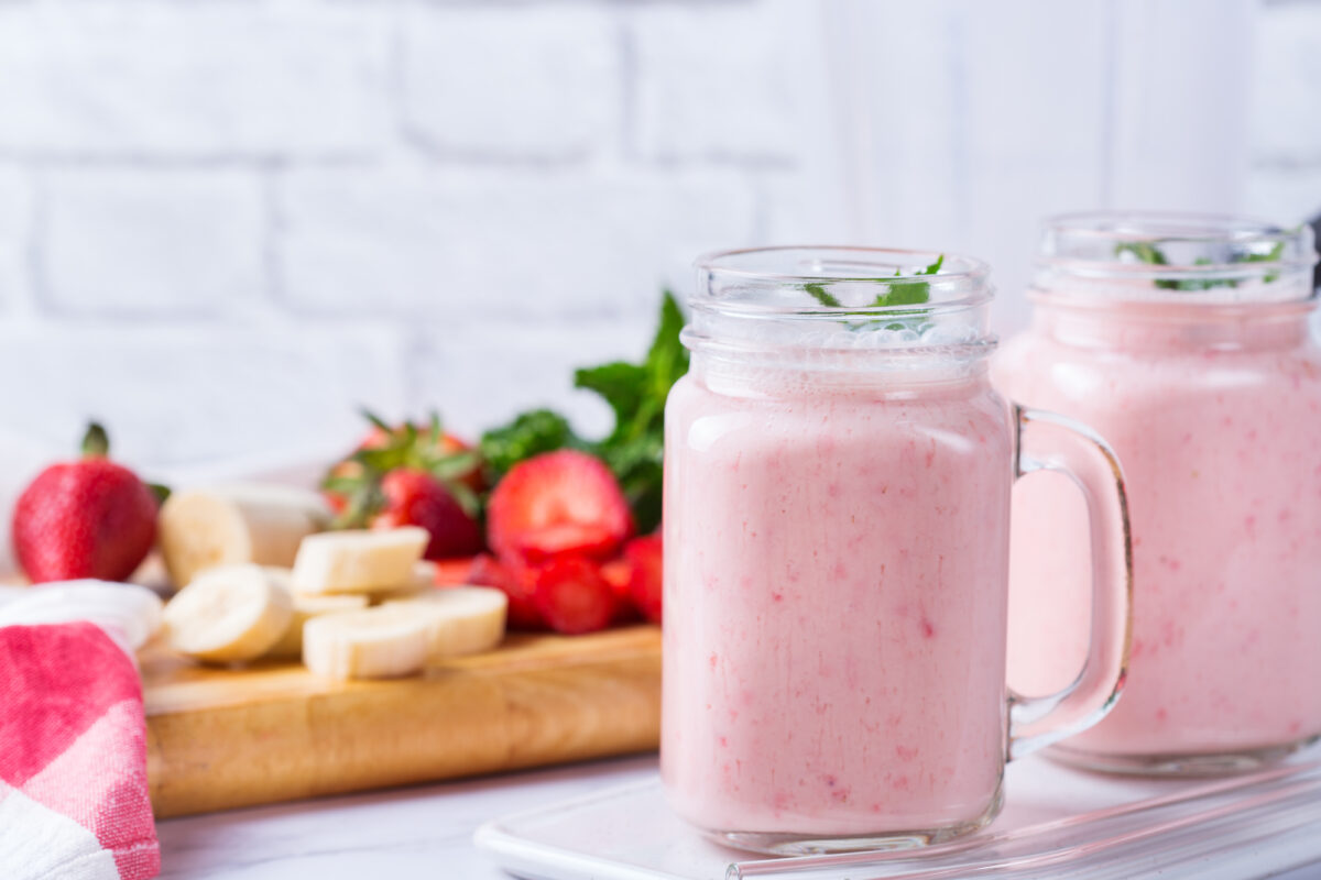 strawberry smoothie in glass jars with fresh strawberries and banans in the background