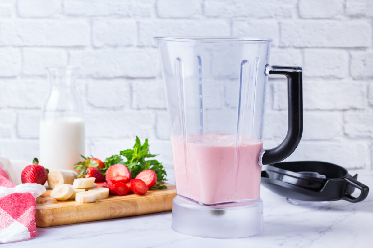 strawberry smoothie in a blender with fresh fruit in the background