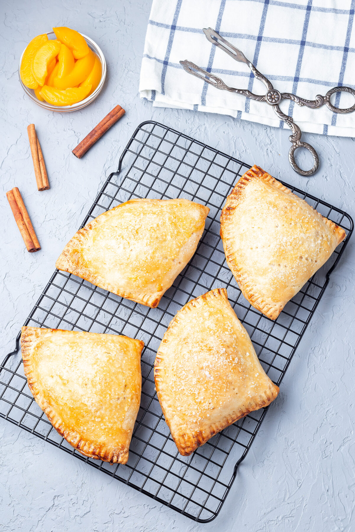 Homemade small peach and cinnamon hand pies with crust dough, sprinkled with sugar, on a cooling rack.