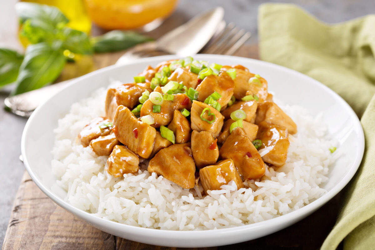 Sweet and sour chicken with rice in white bowl with spring onions