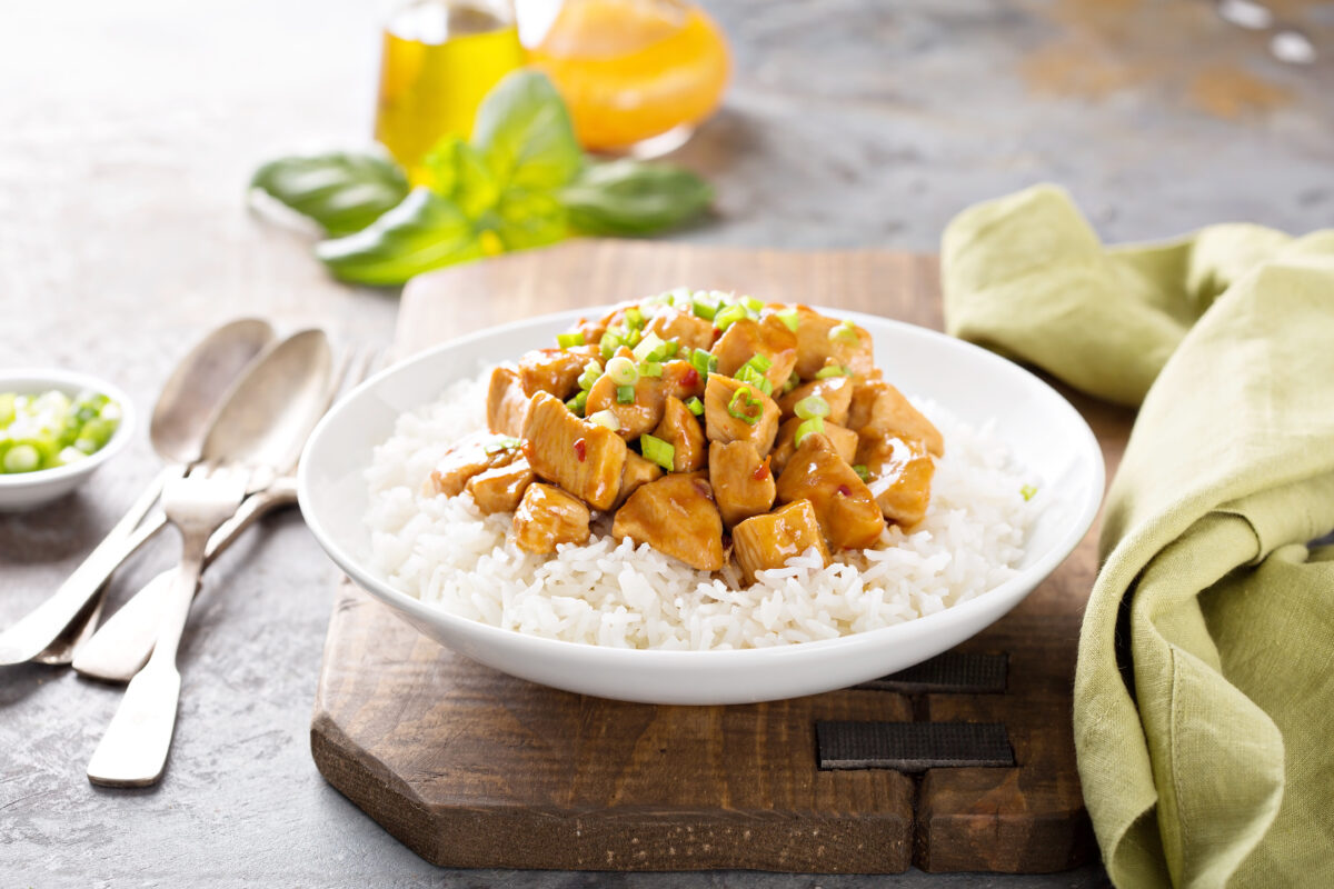 Sweet and sour chicken with rice in white bowl with spring onions