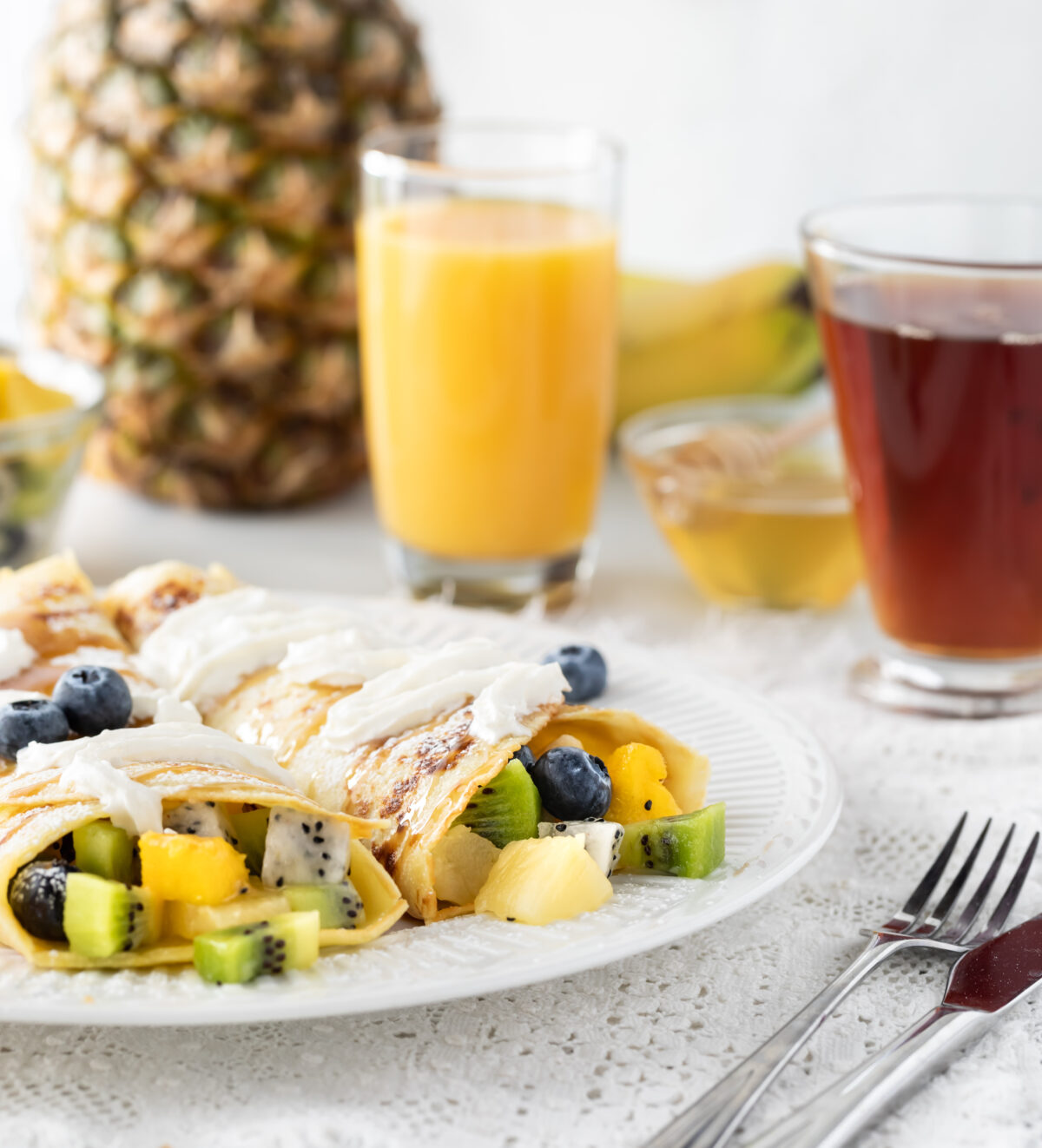 Delicious tropical fruit crepes surrounded by juice, tea and fruit ready for eating.