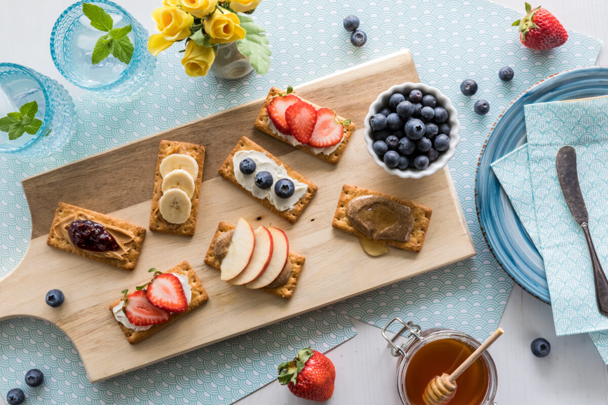 An array of snack crackers with a variety of toppings on a wooden board, ready for snacking.
