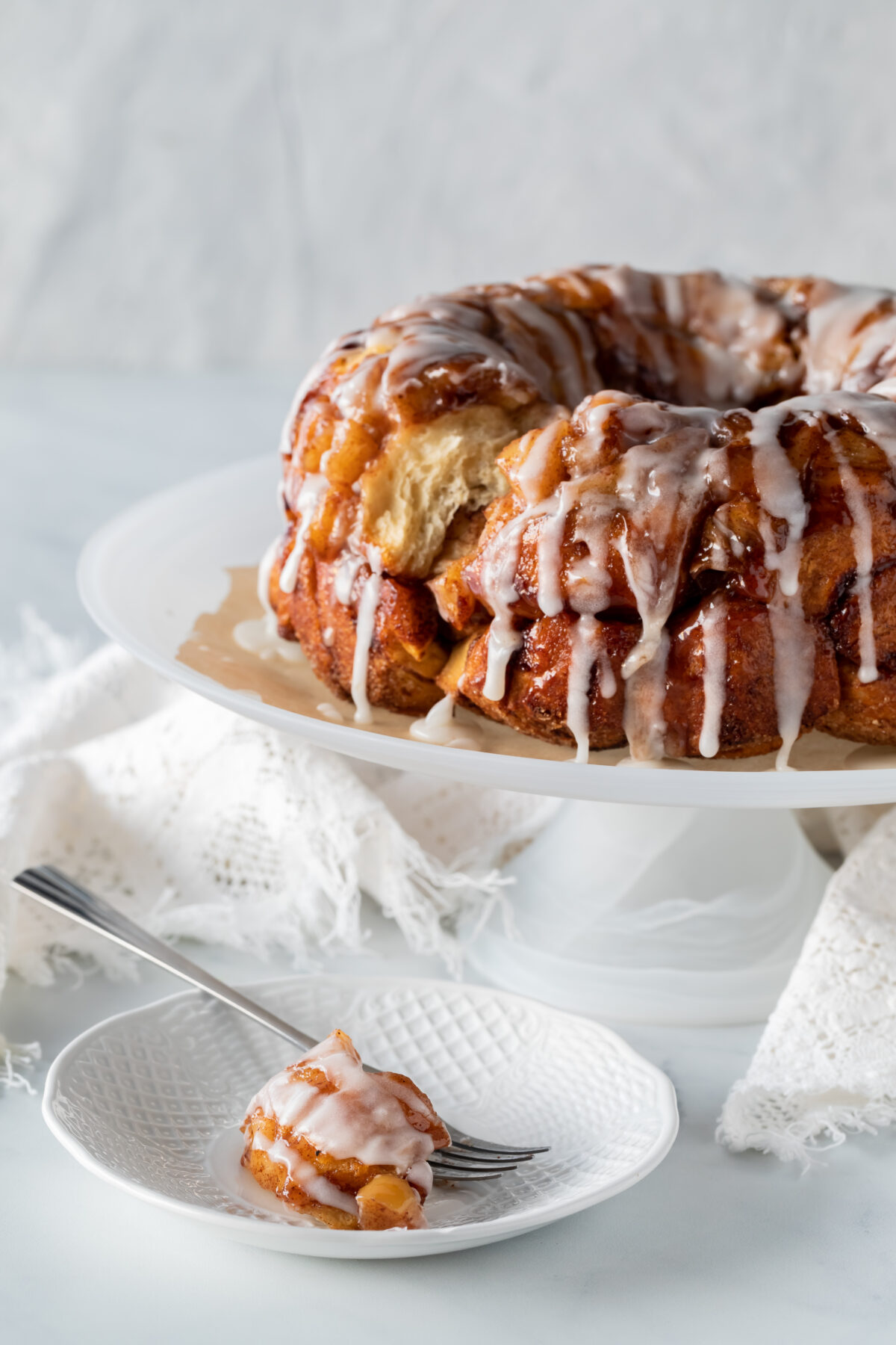 Apple cinnamon pull apart cake on a pedestal stand with a piece on a plate in front.