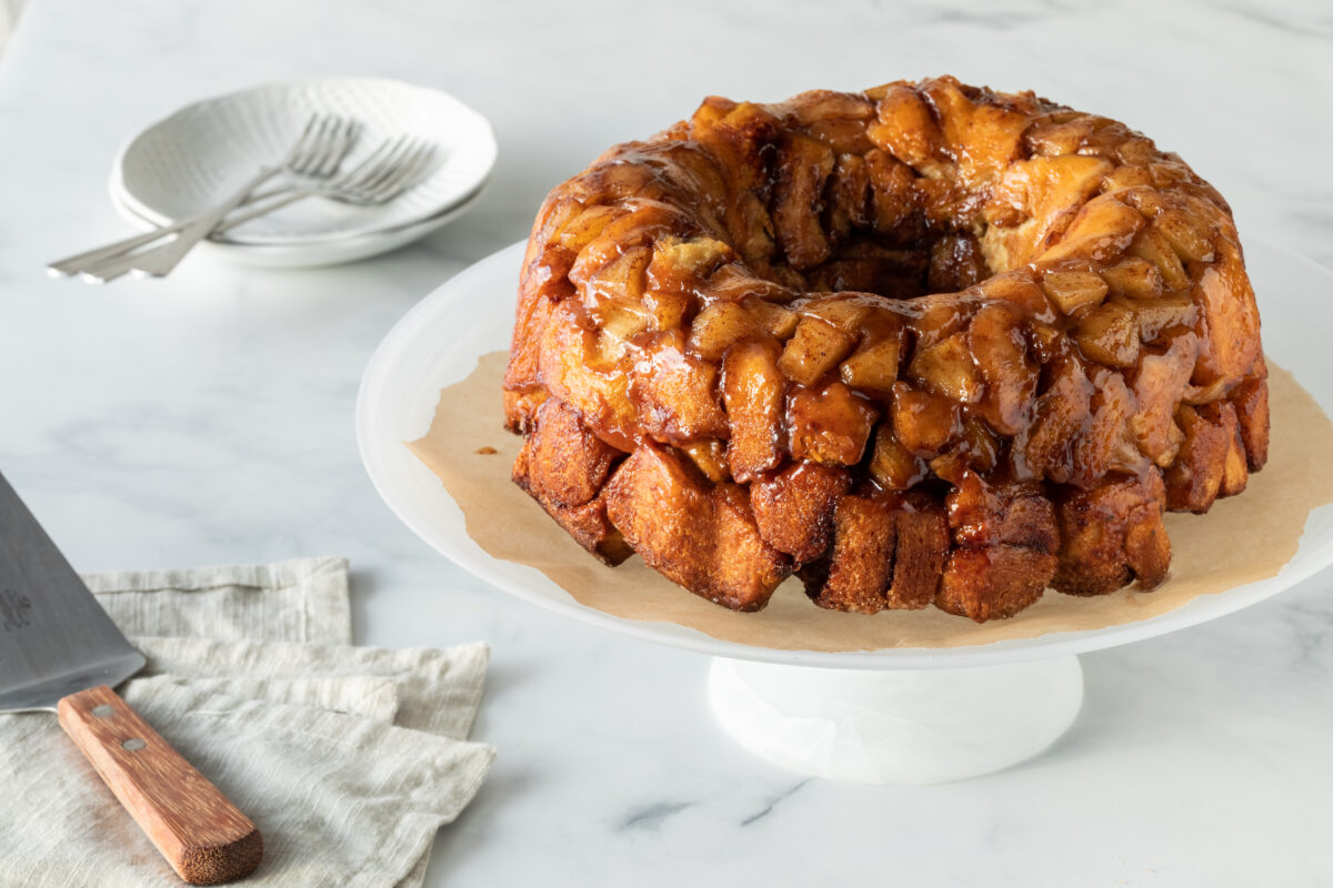A homemade apple cinnamon pull apart bread on a pedestal stand with dishes for serving.