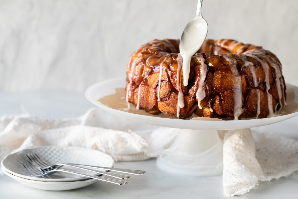Apple cinnamon monkey bread on a pedestal stand with icing sugar being drizzled on top.