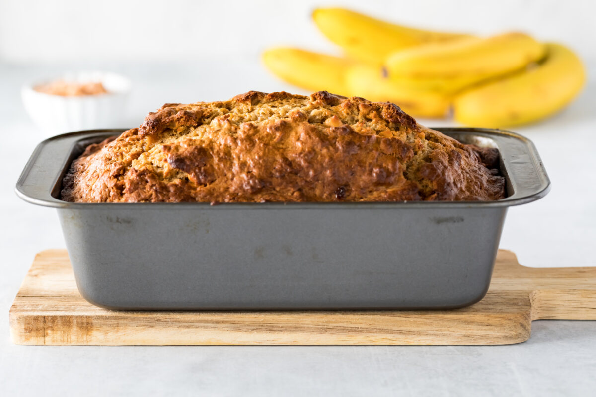 Close up view of a butterscotch banana bread loaf fresh out of the oven cooling on a wooden board.