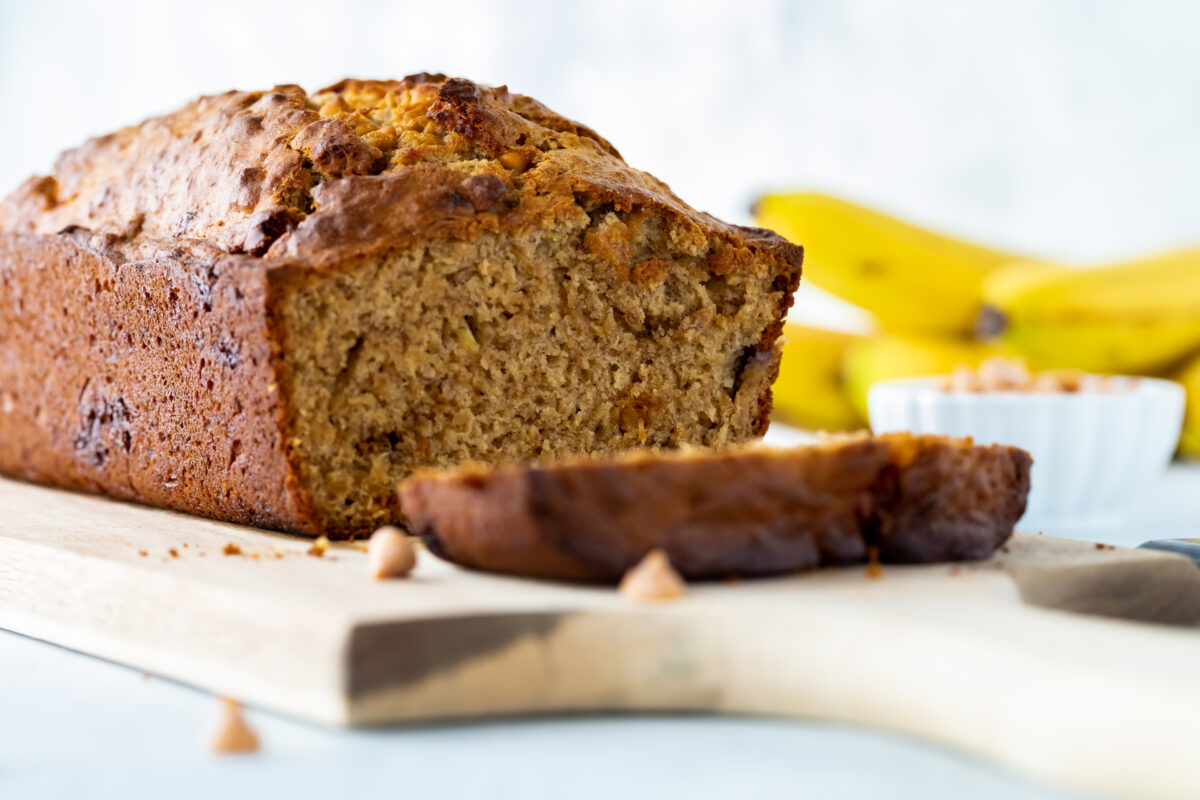 Straight on close up view of butterscotch banana bread with one slice in front, resting on a wooden board.