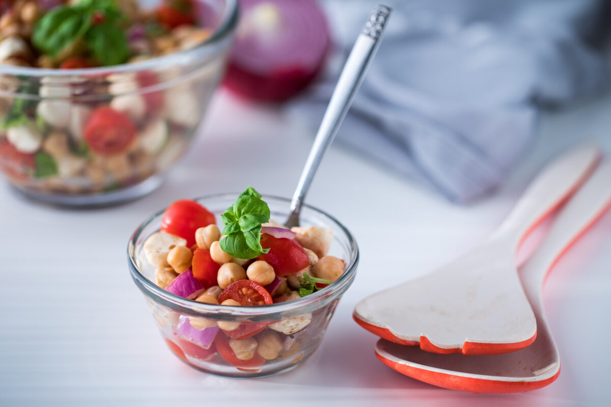 a bowl of chickpea caprese salad in a bowl with tongs