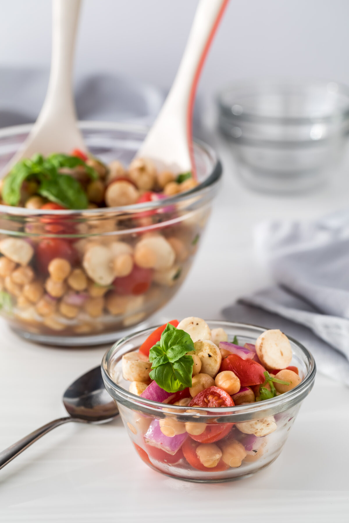 A close up of chickpea caprese salad with a large bowl of salad in behind.