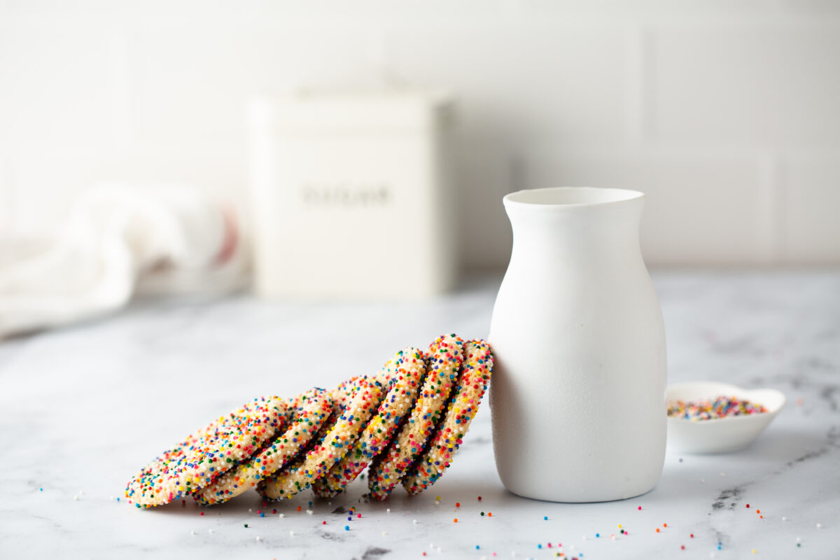 Sugar cookies with sprinkles and a bottle of milk on white background