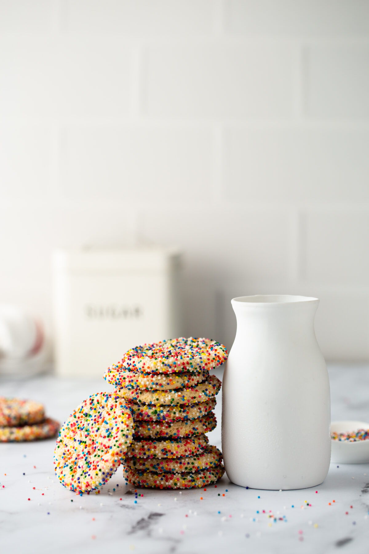 Sugar cookies with sprinkles and a bottle of milk on white background