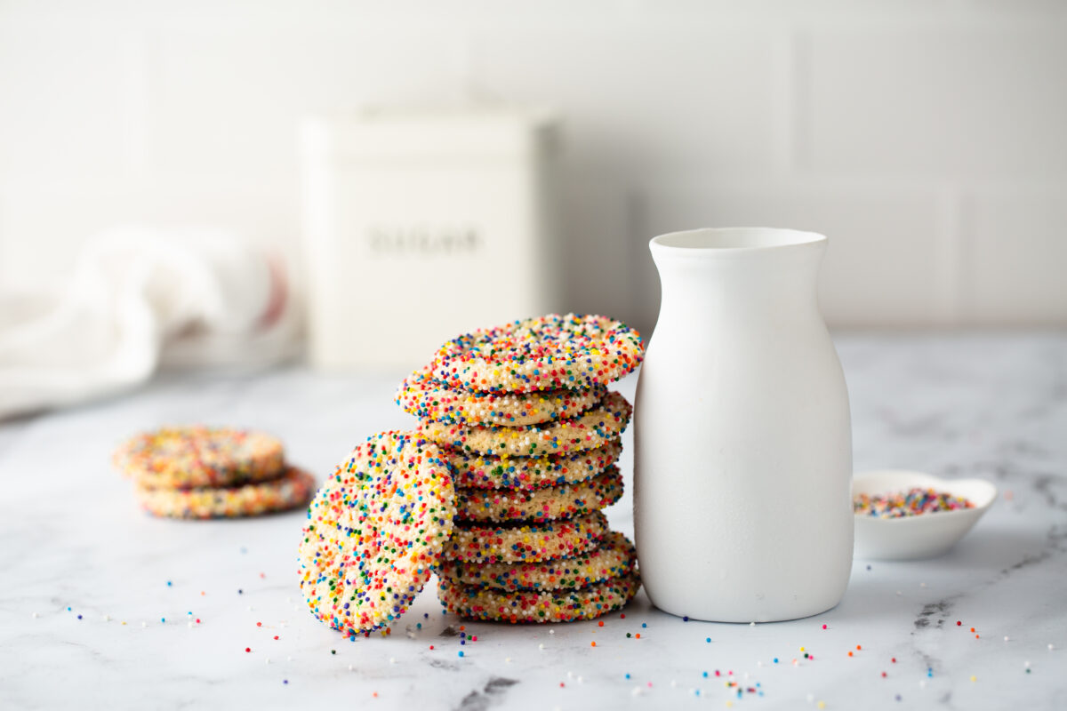 Sugar cookies with sprinkles and a bottle of milk on white background