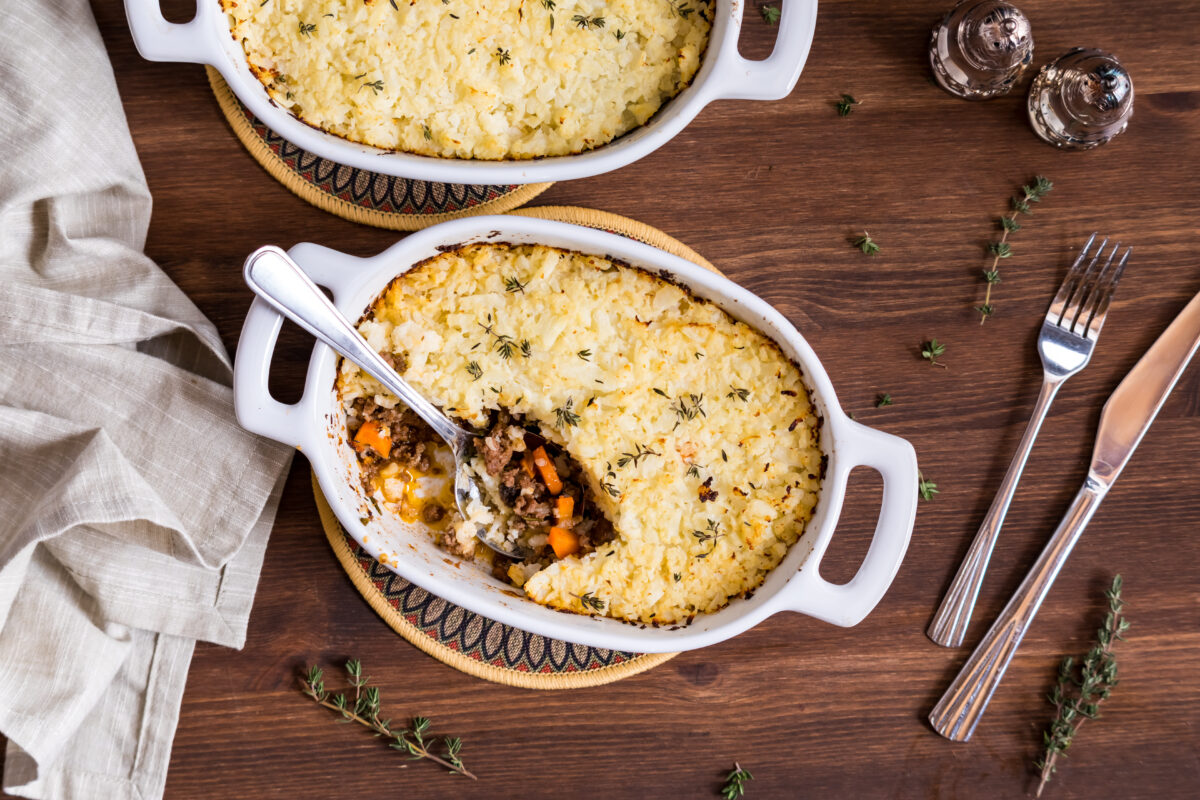 Individual casserole dishes of homemade shepherd's pie topped with mashed cauliflower, ready for eating.
