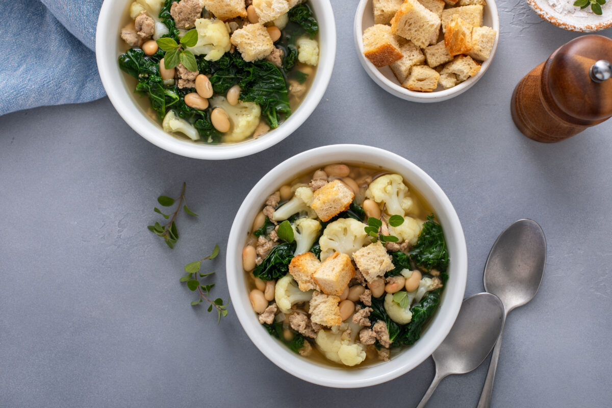 Healthy bean and ground turkey soup or stew with kale and cauliflower, topped with croutons, served in two bowls ready to be eaten