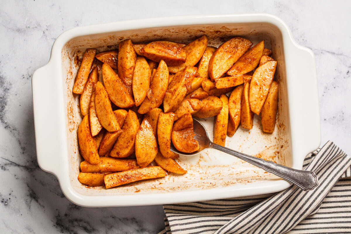 Baked apple slices with cinnamon and maple syrup in a white baking pan.