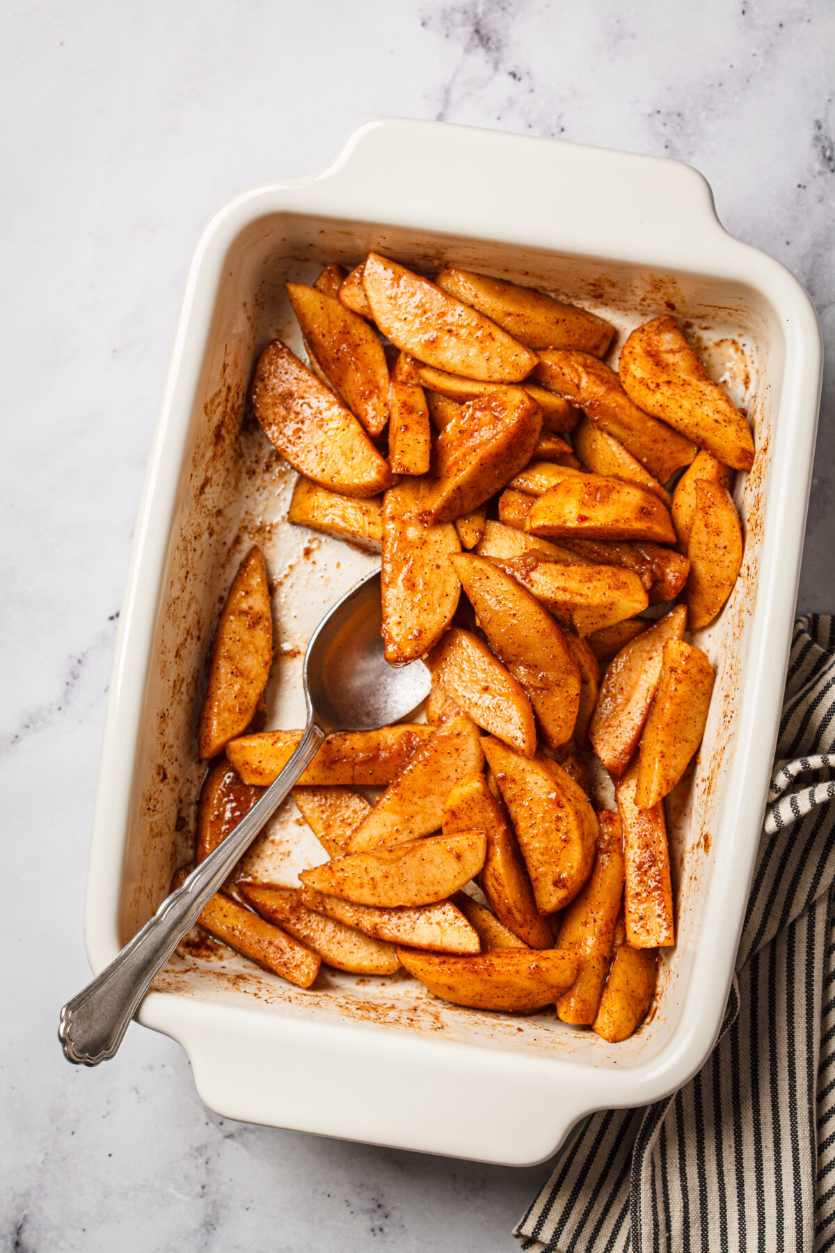 Baked apple slices with cinnamon and maple syrup in a white baking pan.