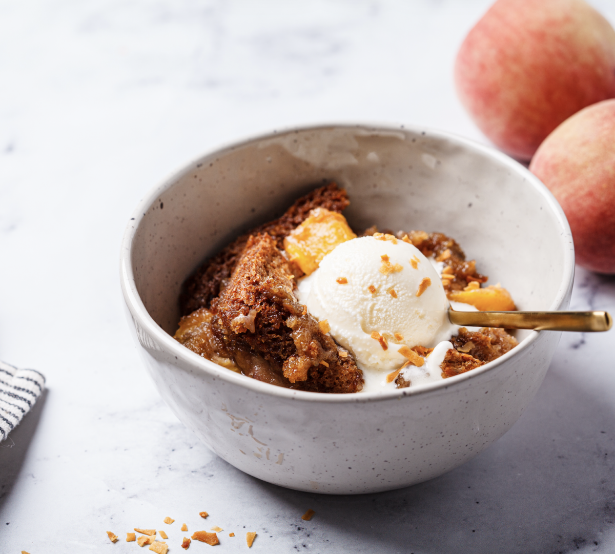 homemade peach cobbler in a serving bowl topped with ice cream