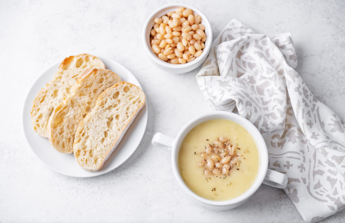 white bean soup in a serving bowl with crusty bread and a linen