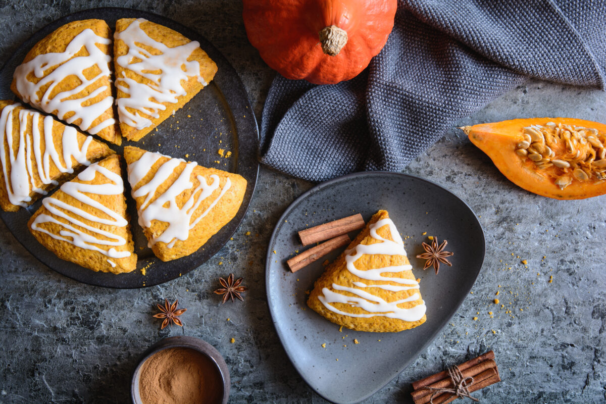 pumpkin scones with maple drizzle cut into wedges on serving plates with spices