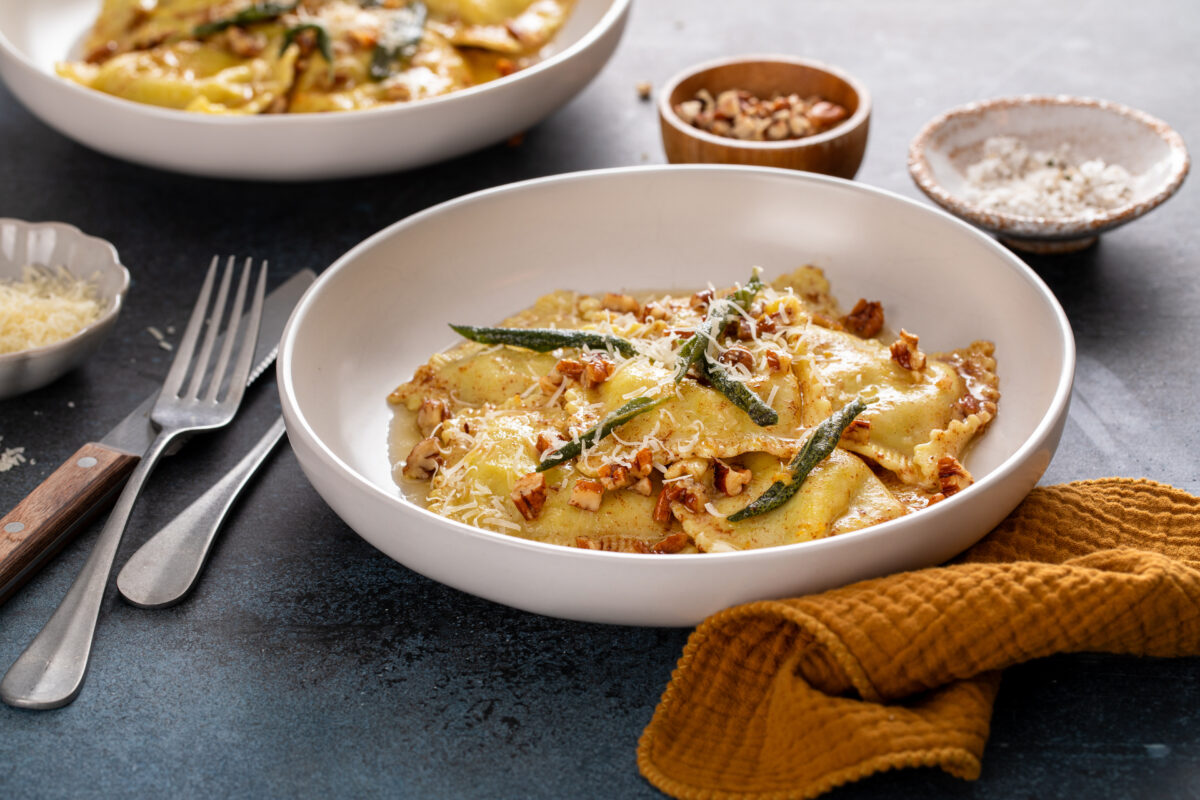 Pumpkin ravioli with brown butter pecan sauce and crispy sage in a serving bowl