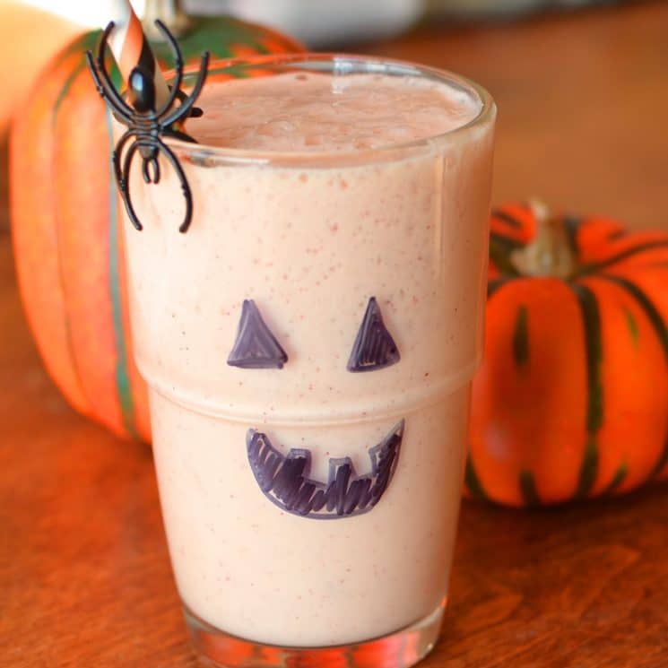 sinaasappelsmoothie in een glas met een jack-o-lantaarn gezicht op getekend