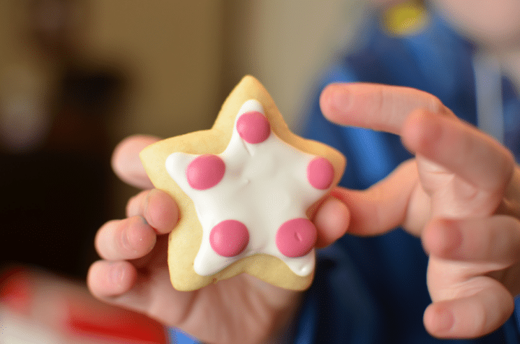close up of child holding christmas cookie in the shape of the star with red and white frosting